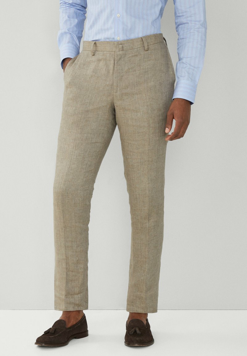 Pantaloni in lino beige con vestibilità dritta, caratterizzati da una parte anteriore piatta e tasche laterali, abbinati a mocassini marroni scuri.