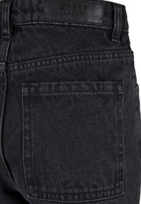 Černé džíny z denimu s texturovaným povrchem, standardními zadními kapsami a koženým logem na pásku. Jednoduchý, klasický design.