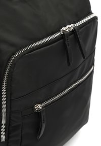Zaino in nylon nero con zip argento, un compartimento principale e una tasca frontale con chiusura con zip aggiuntiva. Superficie testurizzata e design elegante.