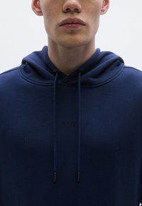 Hanorac bleumarin din material moale, cu șnur, textură striată și un logo subtil "BOSS" în relief pe piept.