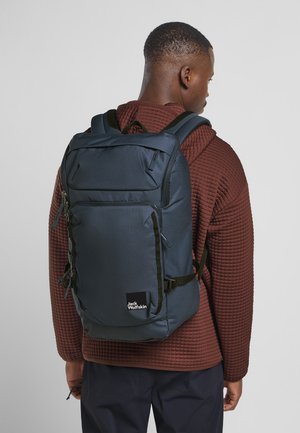 Dark blue backpack with multiple compartments, black hardware accents, and adjustable padded straps. Textured fabric and logo visible.