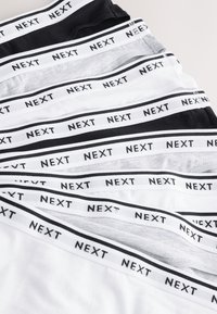 Pile de sous-vêtements noirs, gris et blancs avec des ceintures élastiques où le texte "NEXT" est répété en noir sur des bandes blanches.