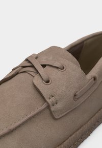 Mocassin en daim beige avec lacets assortis, coutures apparentes et semelle en caoutchouc texturée.