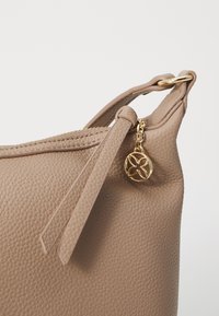 Bolso de mano de cuero beige con una superficie texturizada, cierre con cremallera y un acento decorativo en tono dorado adjunto al tirador de la cremallera.