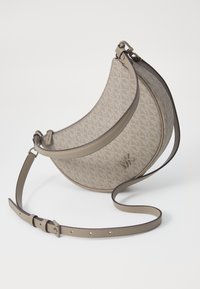 Sac à main beige à motif, de forme arrondie, avec des accents en cuir, une bandoulière ajustable et une fermeture éclair, présentant un logo sur le devant.