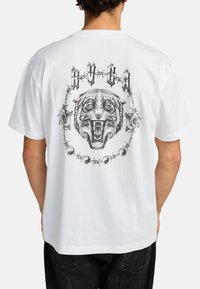 Witte katoenen t-shirt met een grote zwarte afbeelding van een brullende tijger omgeven door een cirkel van rozen en prikkeldraad, met tekst erboven.