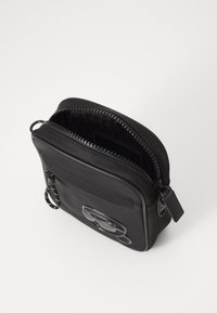Black leather crossbody bag with a zip closure, featuring a textured pattern interior and a branded logo accent on the front.