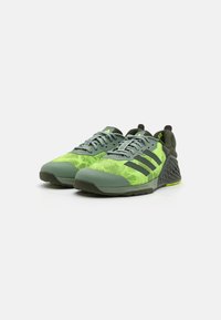 Scarpe sportive a rete verdi e gialle con materiale testurizzato, accenti neri e design a tre strisce. Dotate di un tallone strutturato e suola flessibile.