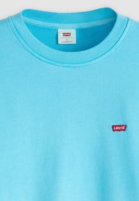 Camiseta Levi's azul claro con cuello redondo, parche del logo de Levi's en rojo en el pecho y etiqueta dentro del cuello que dice "Standard Fit, M".