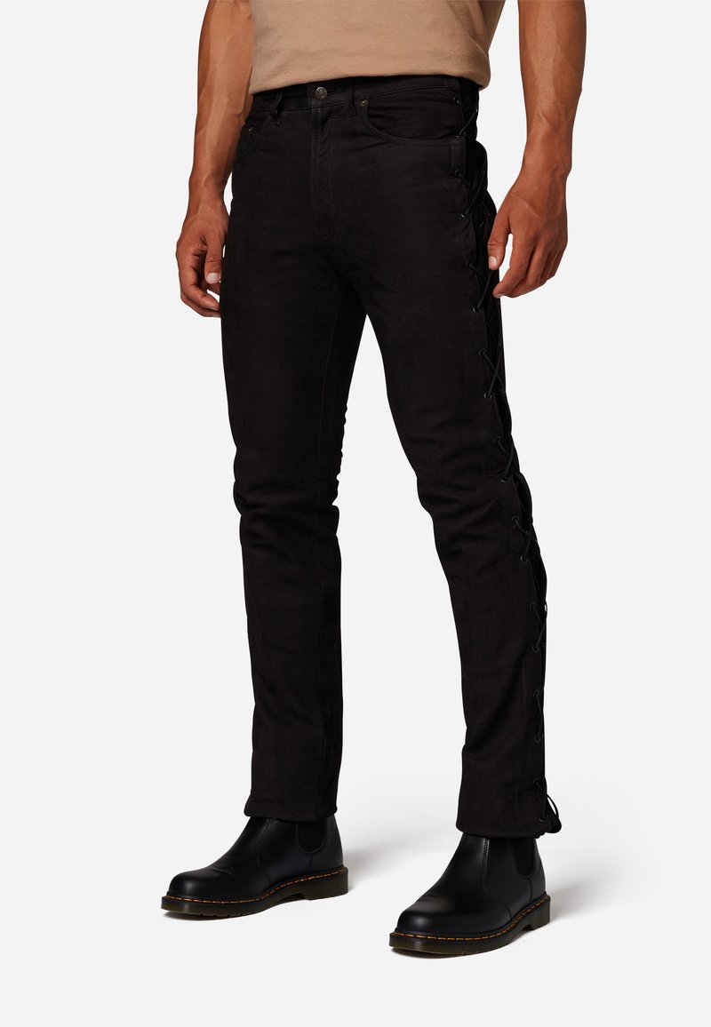 Schwarze Jeans aus Denim mit schmaler Passform, seitlichem Schnürdesign und klassischem Fünf-Taschen-Style. Kombiniert mit schwarzen Stiefeln.