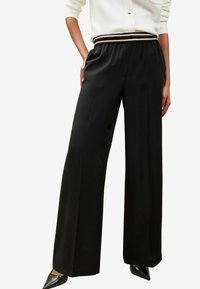 Pantaloni neri a gamba larga con una texture liscia e una cintura elastica a contrasto con strisce dorate e nere.