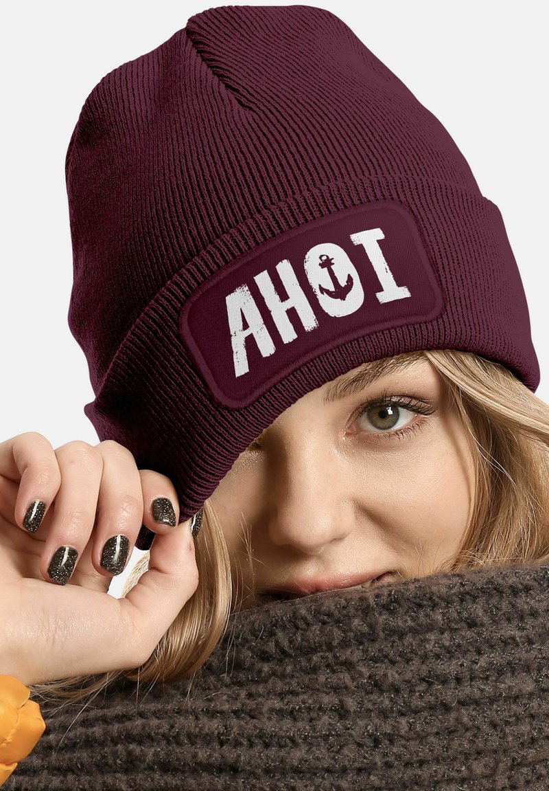 Maroon knit beanie featuring a white patch with the word "AHOI" and an anchor icon. Textured fabric with ribbed design for warmth.
