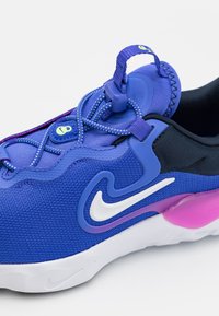 Baskets de sport bleues avec tige en maille texturée, accents violets, logo Nike swoosh blanc, lacets élastiques et semelle blanche rembourrée avec des détails roses.