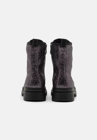 Bottes noires à la cheville en matériau texturé violet, dotées d'une semelle épaisse, d'une fermeture éclair et de poignées à l'arrière.