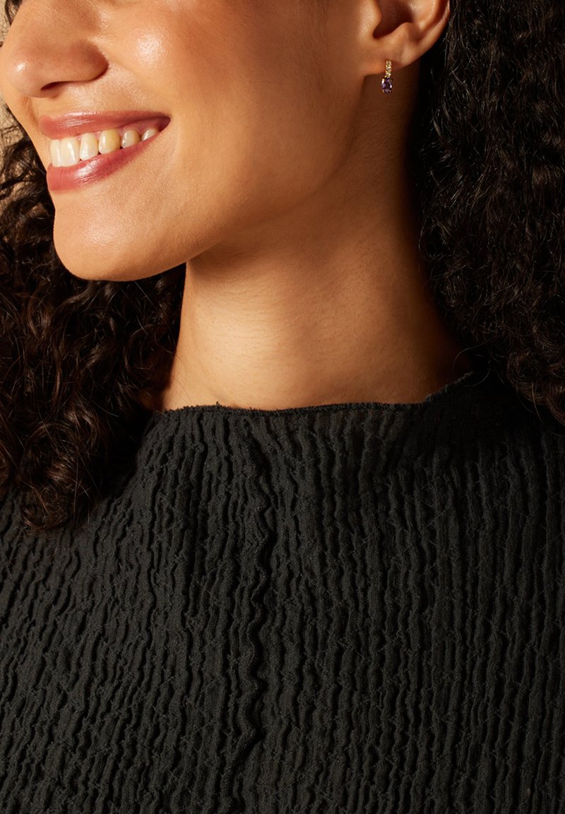 Gouden hoepel oorbellen bevatten een kleine paarse edelsteen en een gestructureerde zwarte blouse met een golvend ontwerp.