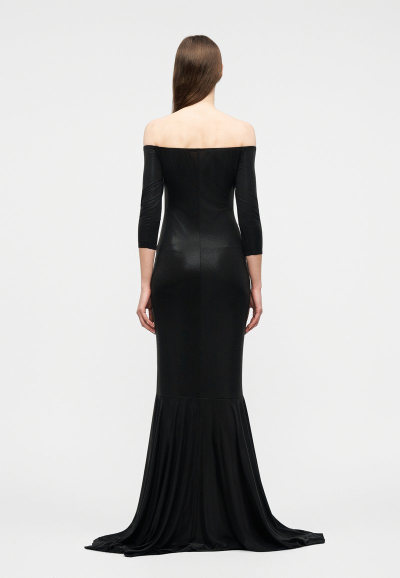 Woman with long hair wearing a fitted black off-shoulder gown with three-quarter sleeves and a flowing train, standing facing away on a plain background.