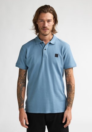 Lichtblauw poloshirt met een gestructureerde stof, korte mouwen en een zwart vierkant logo op de borst. Ontworpen met een klassieke kraag en knopen.