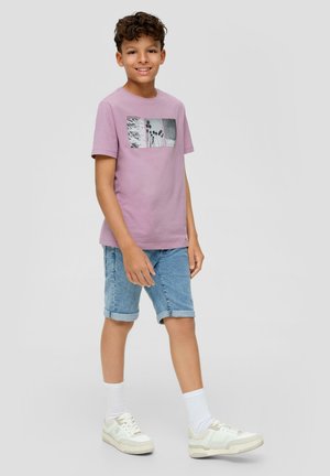 Hellblaues Baumwoll-T-Shirt mit grafischem Druck, kombiniert mit hochgekrempelten Jeansshorts und weißen Sneakers, zusammen mit strukturierten weißen Socken.