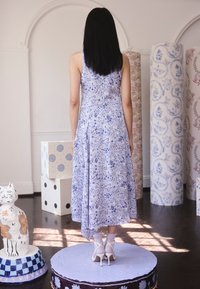 Világoslila virágos ruha légies szabással, lejtős szegéllyel és finom textúrával. Fehér pántos magassarkúval viselve.