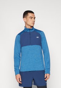 Pullover a maniche lunghe in diverse sfumature di blu, con colletto con zip e pannelli testurizzati a contrasto. Presenta un piccolo logo sul petto.