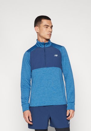 Sudadera de manga larga en diferentes tonos de azul, con cuello con cremallera y paneles texturizados en contraste. Presenta un pequeño logo en el pecho.