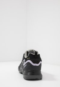 Zapato de senderismo impermeable en negro y gris con parte superior de malla, talón reforzado y suela texturizada. Presenta un logo de Gore-Tex y la marca Terrex.