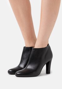 Sorte læderankelstøvler med en glat tekstur, rund tå og en slank høj hæl. Har lynlåsbagpå.
