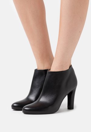 Bottines en cuir noir à texture lisse, bout arrondi et talon aiguille fin. Dotées d'une fermeture éclair à l'arrière.