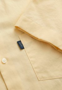 helekollase särgi varrukas ja esitasku, millel on kreemikas nupp ja väike tumesinine brändimärk, millel on homaarisümbol.