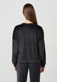 Felpa in velluto nero con maniche lunghe, vestibilità rilassata e polsini a costine. Texture liscia con un design semplice, senza motivi o accenti visibili.