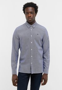 Blau gemusterte Bluse mit Kragen, langen Ärmeln und einem subtil strukturierten Stoff. Verfügt über sichtbare Knöpfe und ein kleines Logo.