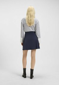 Bluzka w paski z długimi rękawami i białymi mankietami, zestawiona z granatową spódnicą w fasonie dzwonowym. Modelka ma na sobie czarne botki za kostkę na słupku.