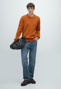 Pomarańczowy sweter dzianinowy, niebieskie dżinsy, czarna torba i brązowe buty. Sweter ma okrągły dekolt; torba ma luźny fason; dżinsy są prostego kroju.