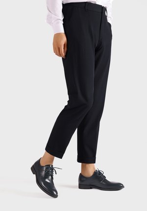 Zwarte op maat gemaakte broek met een slim fit en opgerolde boorden, gecombineerd met donkere leren veterschoenen. Glad stof, minimalistisch design.