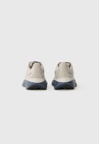 Pair of beige running shoes with dark blue soles viewed from the back on a plain white background.