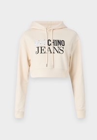 Zrezaná béžová mikina s kapucňou, z mäkkého materiálu, dlhé rukávy, s nastaviteľnými šnúrkami, s čiernym grafickým nápisom "MOSCHINO JEANS" v tučnom písme.