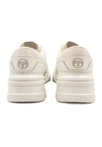 Světle béžové tenisky s texturovaným povrchem, polstrovaným límcem a značkovým akcentem. Mají silnou podrážku se jemnými vodorovnými proužky a perforacemi.