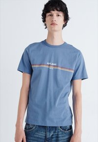 Kék pamut póló, kerek nyakkal, rövid ujjakkal, piros, sárga és zöld vízszintes csíkkal, rajta "PEPE JEANS" felirattal.