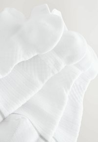 White cotton socks featuring a textured pattern and ribbed cuffs, stacked with smooth, rounded toes and a simple gray accent line.