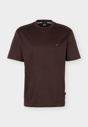 Plain dark brown short-sleeve crew neck t-shirt with small round logo on left chest and black brand tag on side seam.