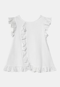 Biała bawełniana bluzka z falbankami z ażurowej koronki, okrągłym dekoltem i rozkloszowanym kształtem. Falbanki biegną wzdłuż ramion i dolnego brzegu.