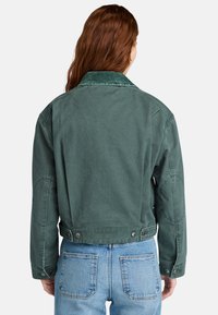 Groene canvas jas met een corduroy kraag, drukknoopsluiting en een cropped design. Heeft gestikte mouwnaden en een gladde textuur.