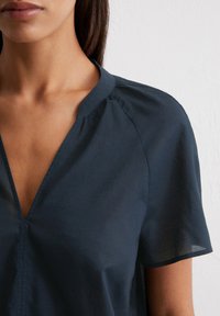 Navy blue blouse with a V-neck, short sleeves, and gathered detail at the shoulders, made from a lightweight, slightly sheer fabric.