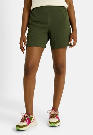 Pantalones cortos verdes, ligeros, con una cinturilla elástica, textura suave y un diseño sencillo. Combinados con zapatillas deportivas multicolores.