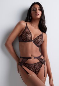 Ensemble en dentelle comprenant un bralette et un string en brun avec un motif léopard, présentant des bords festonnés, des accents dorés et des bretelles ajustables.