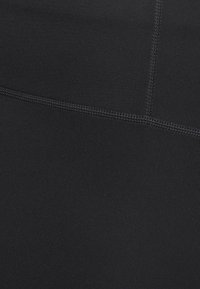 Närbild av svart tyg med synlig tätt sömnad som formar en vinklad söm på en slät textilyta.