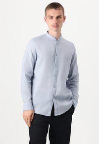 Lyseblå langermet skjorte med krageband, frontlukning med knapper og et mykt, strukturert stoff. Brukt med svarte bukser.