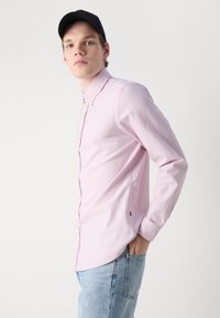 Lichtroze lange mouwen shirt met een button-down kraag, slim fit en subtiele stikdetails, gecombineerd met lichtblauwe denim jeans.