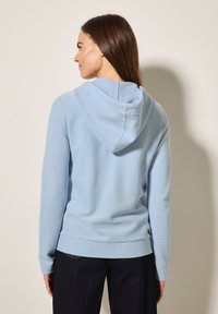 Felpa con cappuccio azzurro chiaro, caratterizzata da una texture a coste e una vestibilità comoda, dotata di tasca a marsupio e maniche lunghe.
