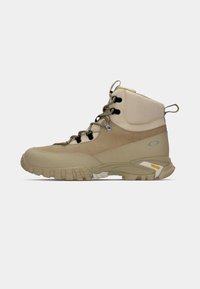 Stivale da trekking beige con caviglia alta, materiale in suede e tessuto testurizzato, suola in gomma robusta e lacci neri. Presenta il marchio Vibram.